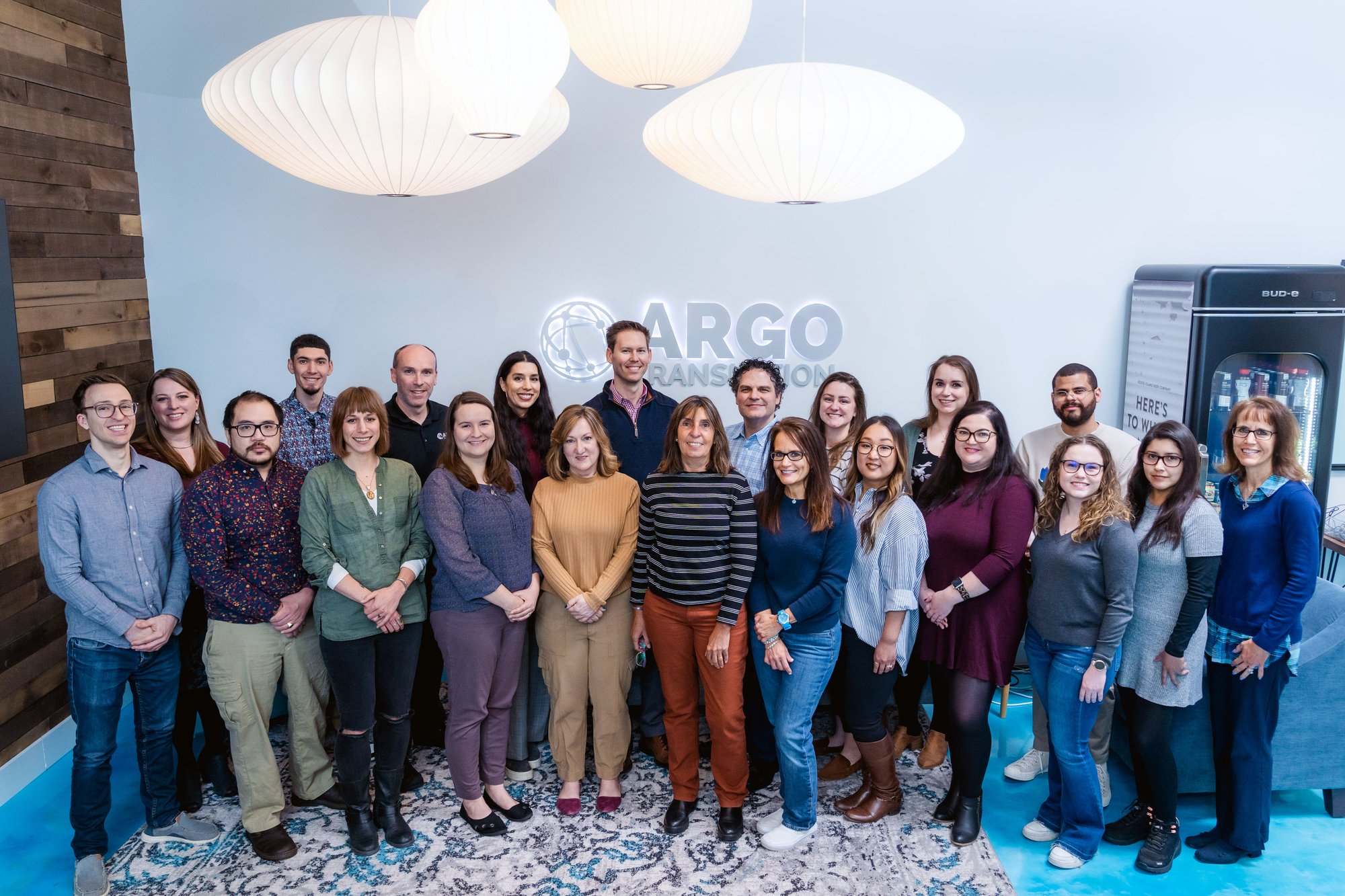 The Argo Translation team standing together in the office beneath the company's illuminated wall logo