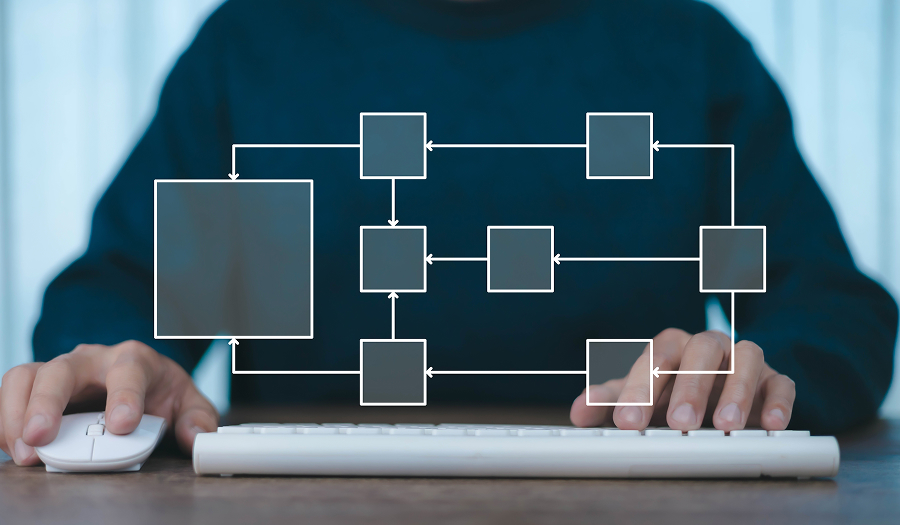 A person seated at a desk using a keyboard and mouse, with a translucent workflow diagram of connected boxes overlaid in the foreground.