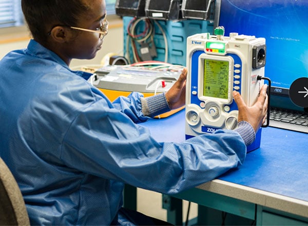A ZOLL technician testing a portable ventilator at a workbench