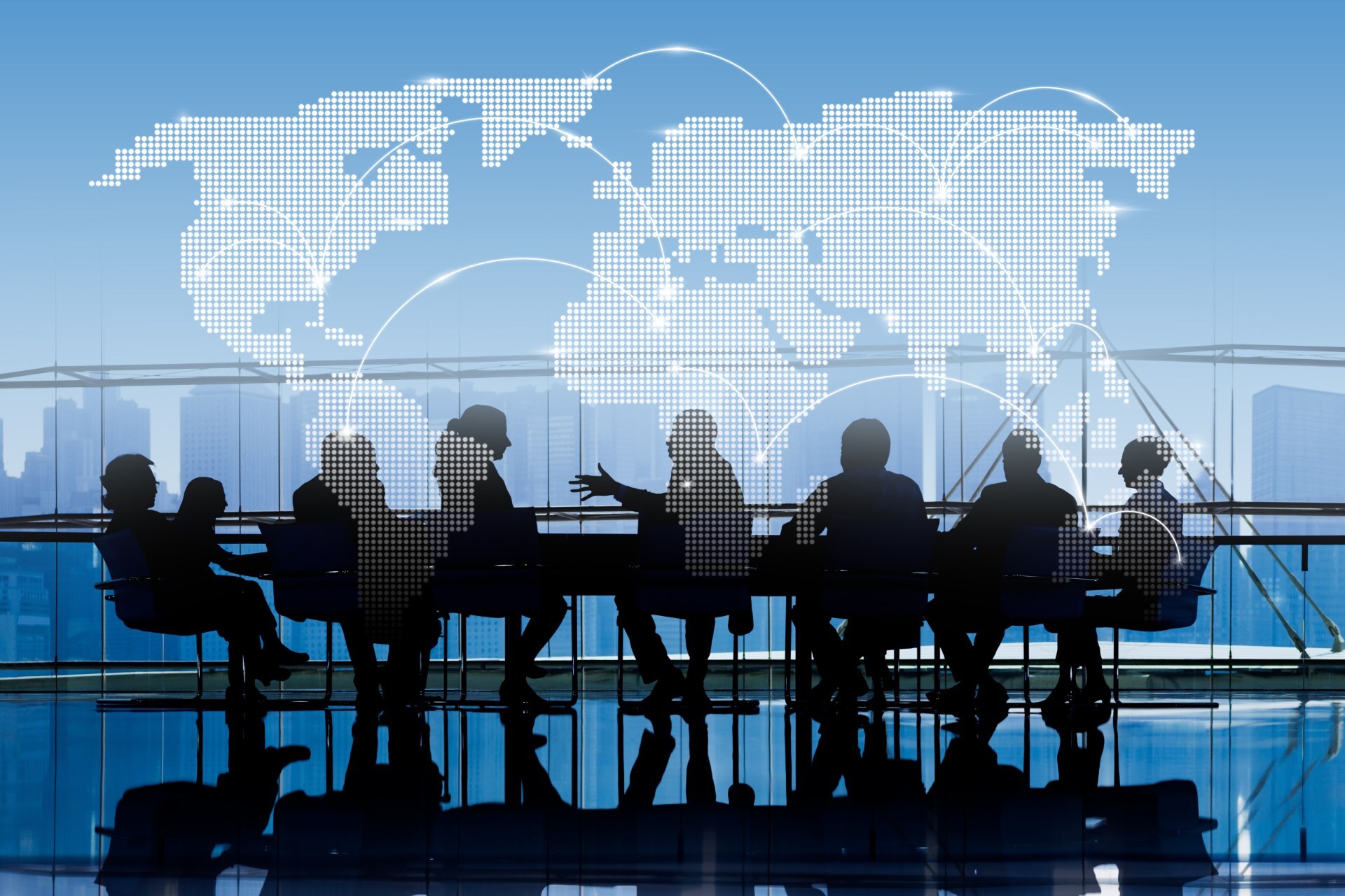 Silhouetted team meeting at a boardroom table beneath a dotted world map
