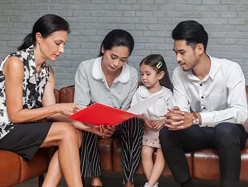A school staff member reviewing documents with two parents and their young child
