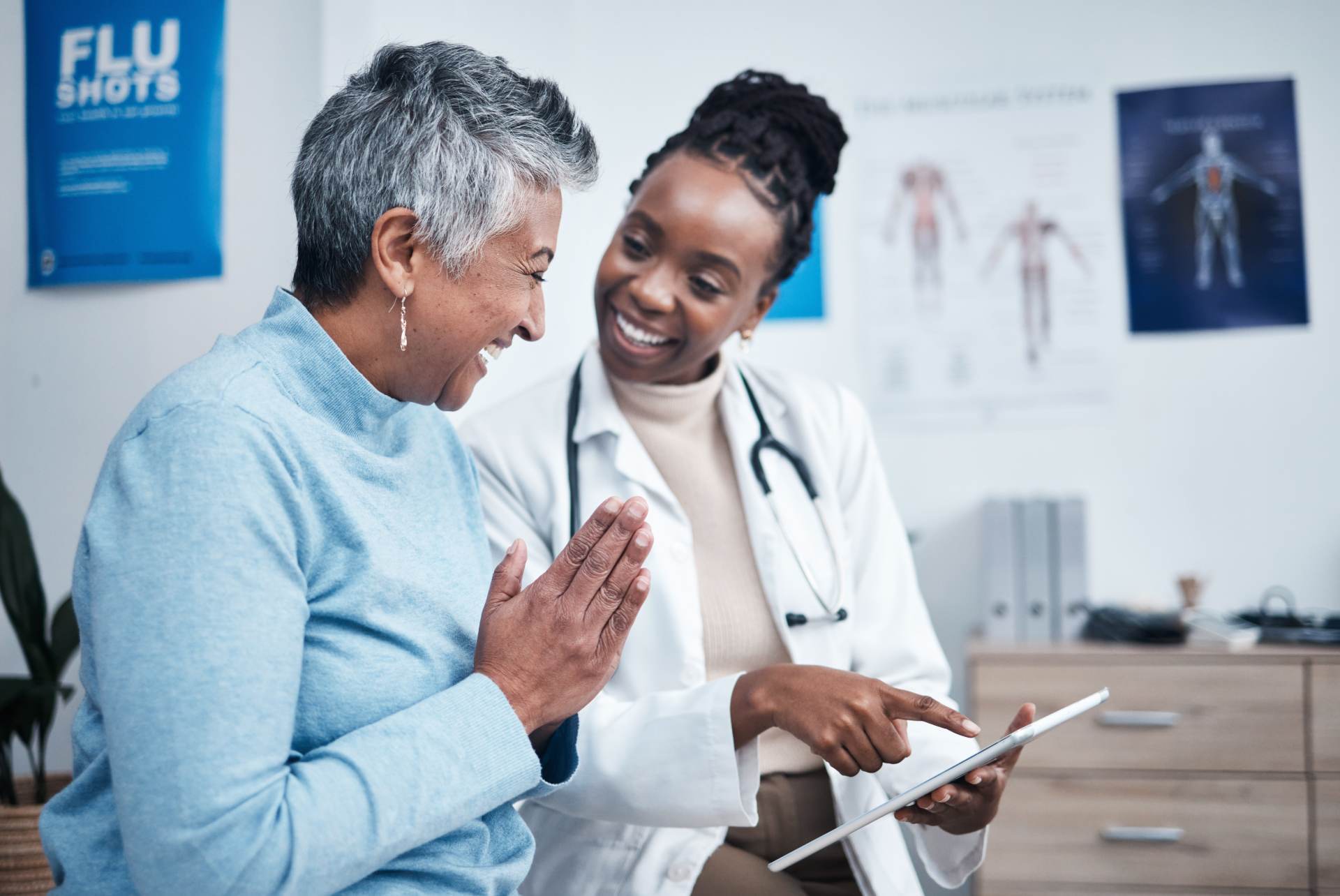 A doctor showing a tablet to a smiling senior patient in an exam room