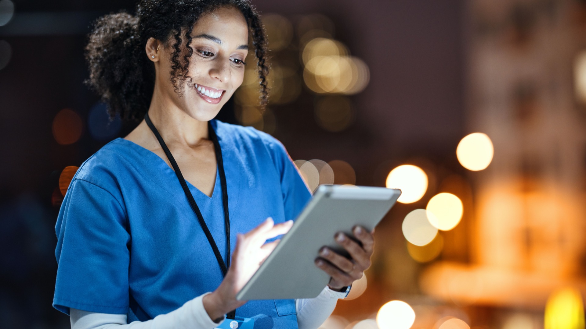 A nurse in blue scrubs using a tablet during a night shift