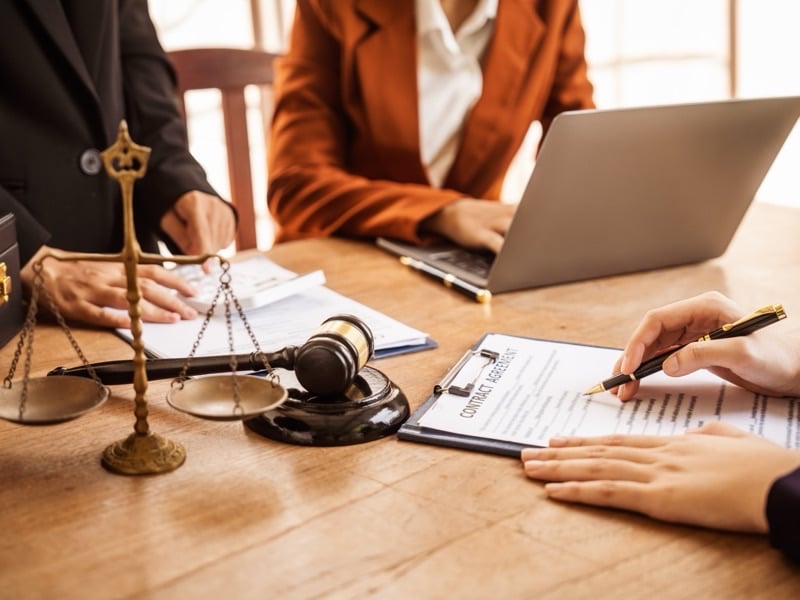 A lawyer and client reviewing a contract beside a gavel and scales of justice