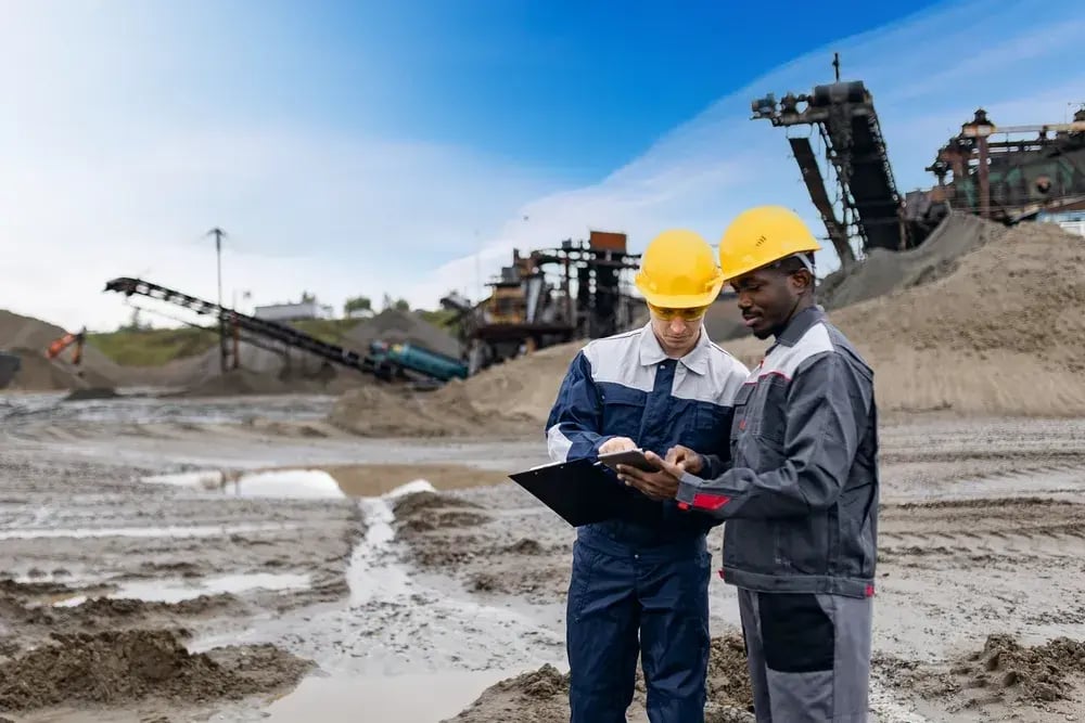 Two mining workers in hard hats reviewing a tablet at a mine site