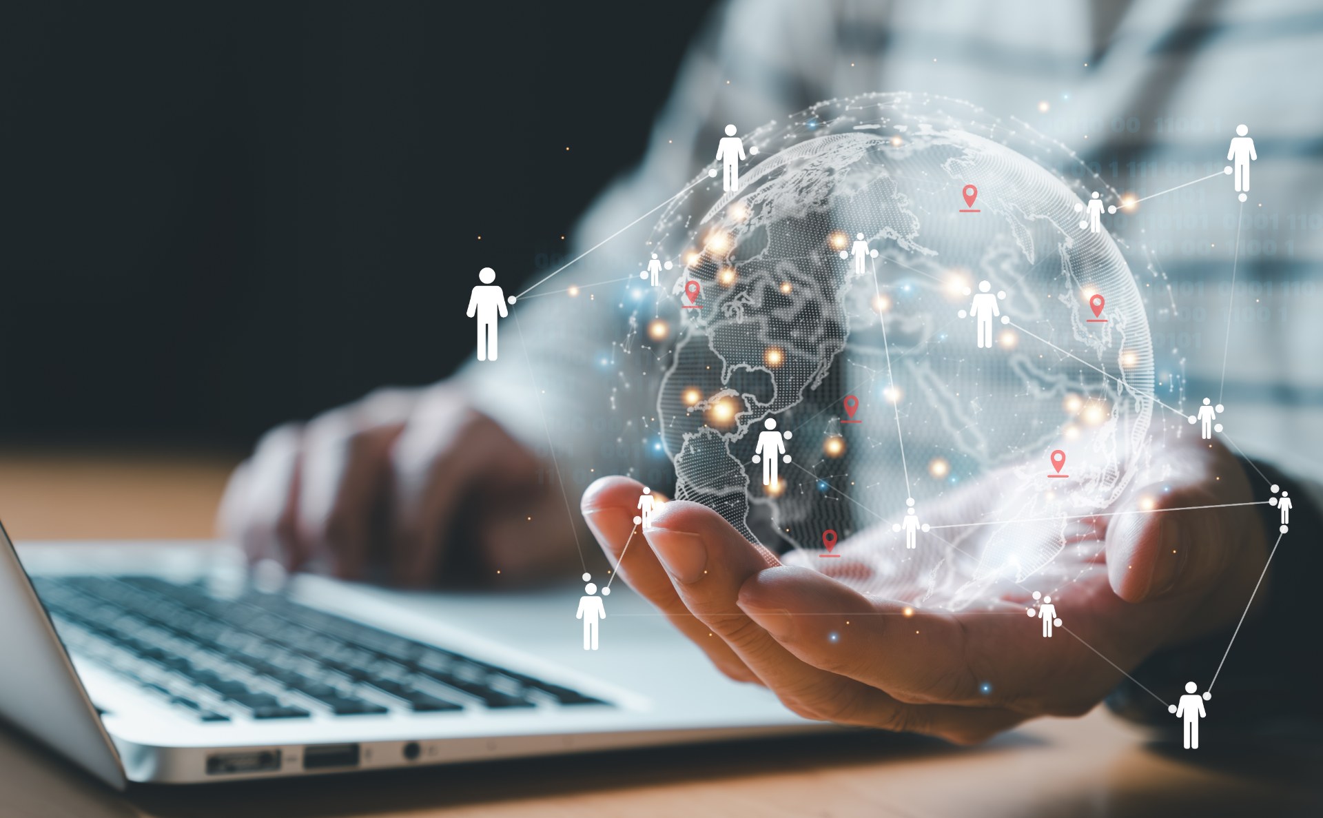 Person at a laptop holding a glowing globe in an open palm, ringed by person icons and location pins linked into a network