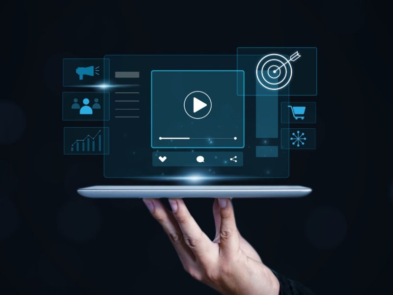 A hand holding a tablet with a glowing video player and marketing icons floating above it