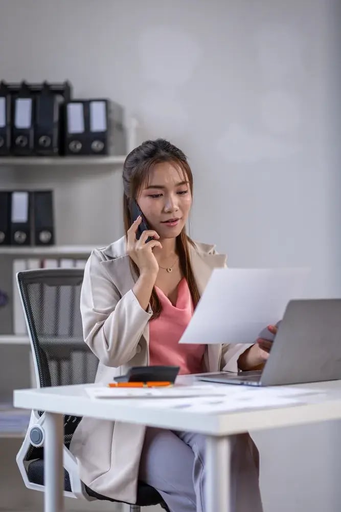 Office worker on a phone call reading a printed document at a desk