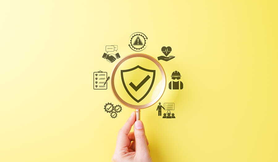 Magnifying glass over a safety shield icon surrounded by workplace safety symbols including a construction worker, checklist, warning sign, and handshake on a yellow background.