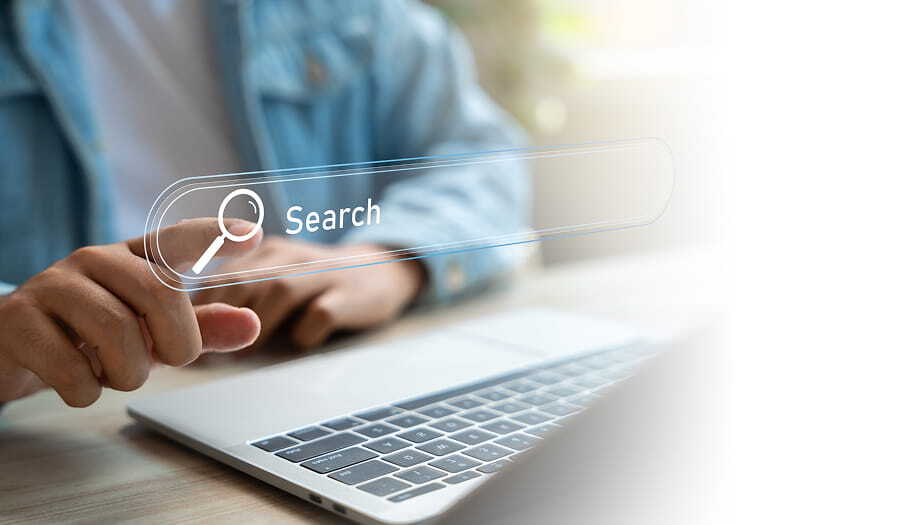 Person using a laptop with a floating search bar graphic on the screen.
