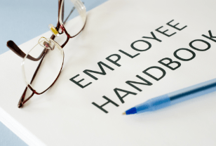 An employee handbook on a desk beside reading glasses and a pen
