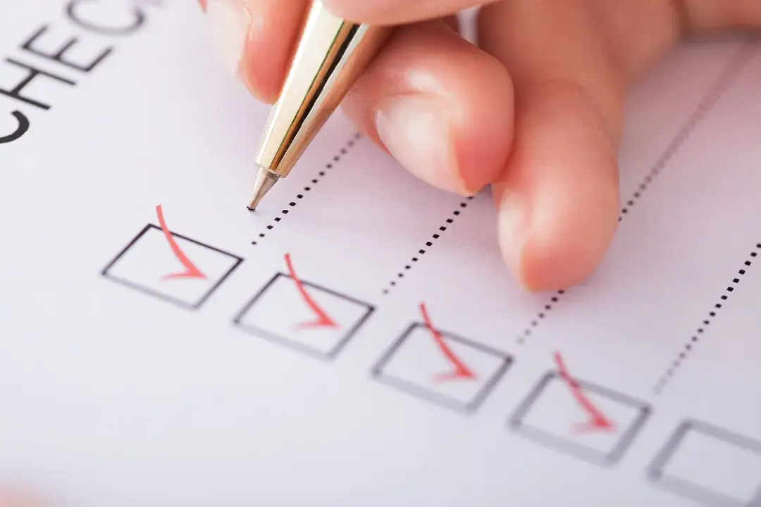 A hand using a pen to check off boxes on a printed checklist