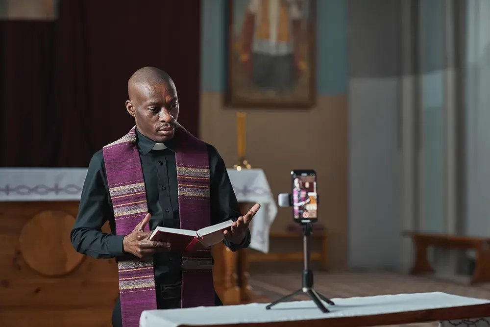 A pastor reading from a book while a phone on a tripod streams the service