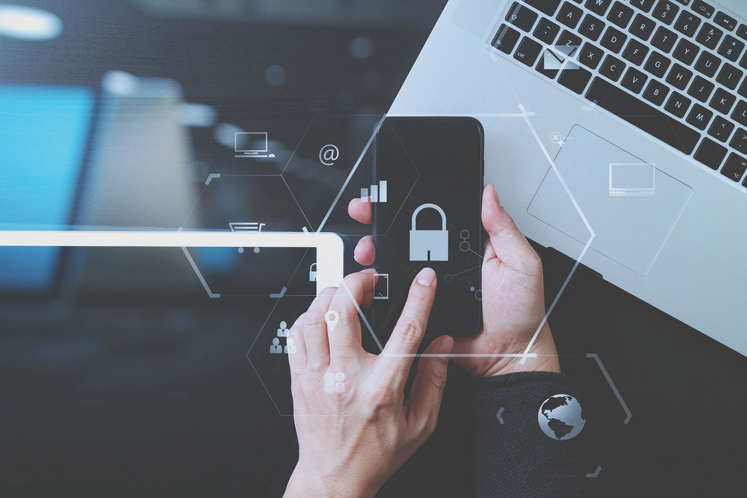 Hands holding a phone showing a padlock icon, beside a laptop