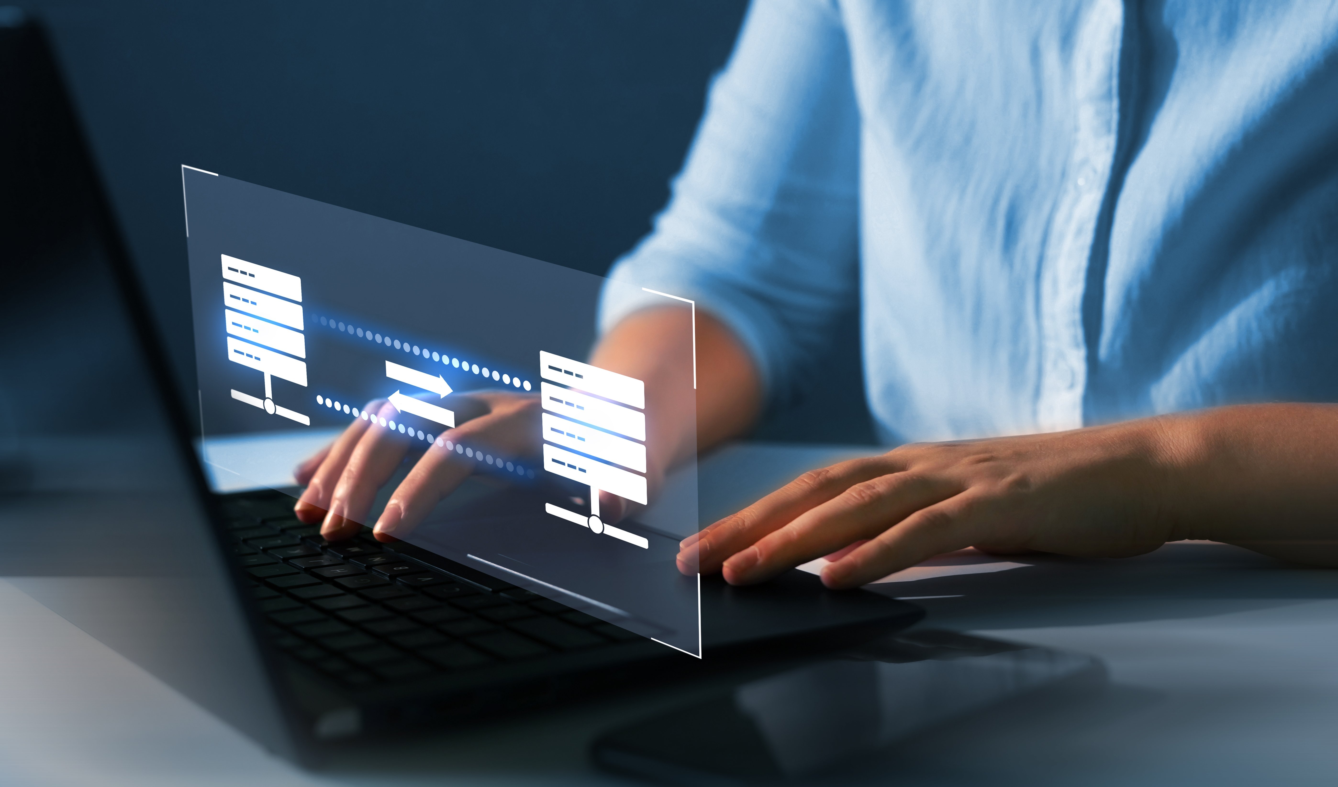 Person typing on a laptop with a graphic of data syncing between two servers