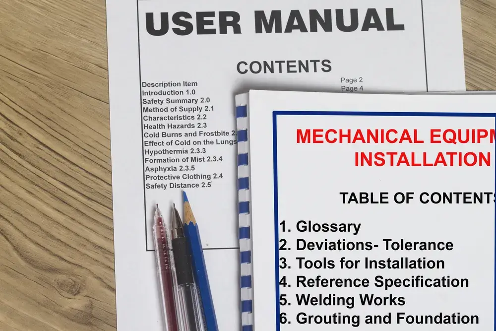 A printed user manual and an equipment installation manual lying on a desk with pens